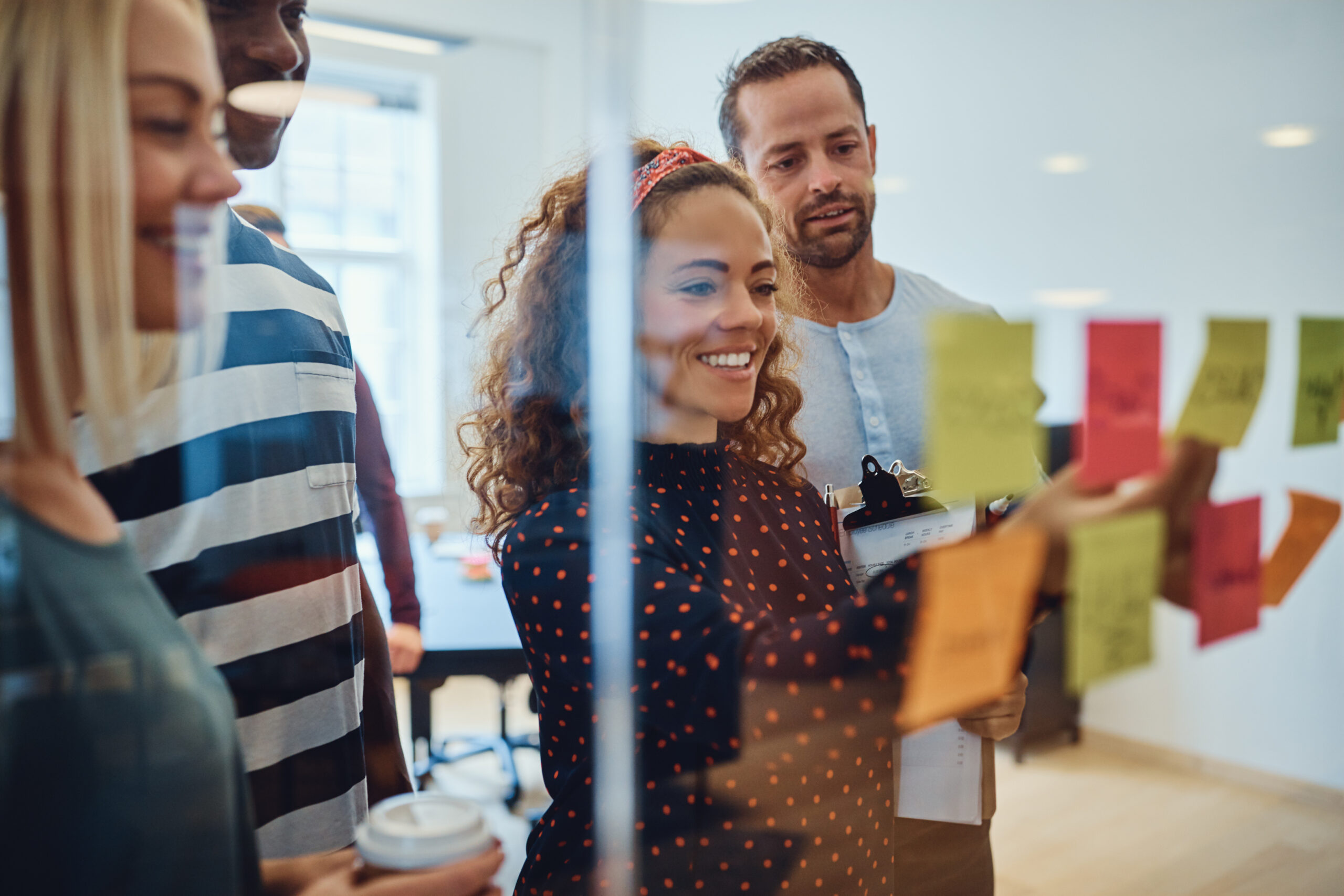 Smiling,Group,Of,Designers,Reading,Sticky,Notes,On,A,Glass
